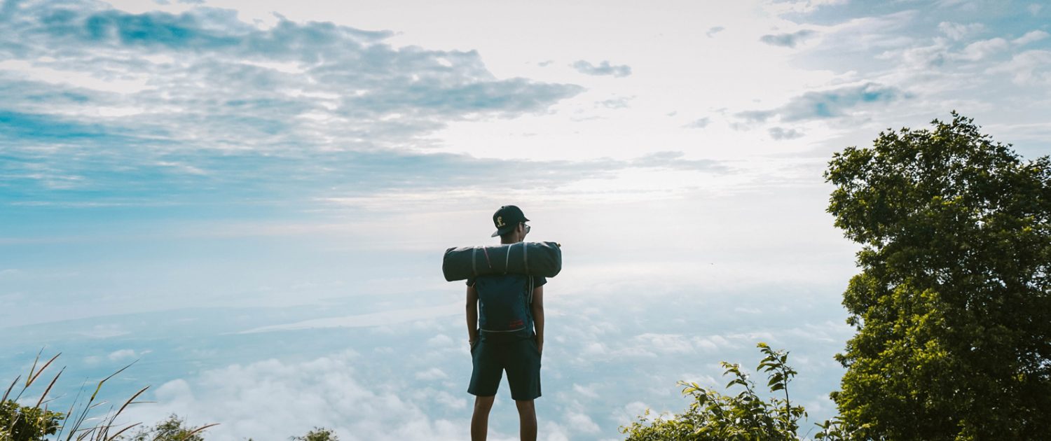 Un chico de espaldas con una mochila en la cima de una montaña y nubes de fondo