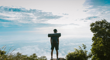 Un chico de espaldas con una mochila en la cima de una montaña y nubes de fondo